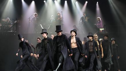 Groep mensen in zwarte kleding, deels met hoge hoed op, die en groupe een kant op lopen.