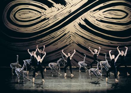 Ensemble van dansers op het podium met op de achtergrond een zwart met beige grafische print