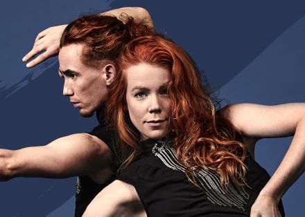 Vergrijsd-blauwe afbeelding met daarop twee personen met rood haar. De vrouw vooraan heeft een arm op haar heup en leunt naar achteren. Achter haar staat een man met zijn armen als pijl en boog.